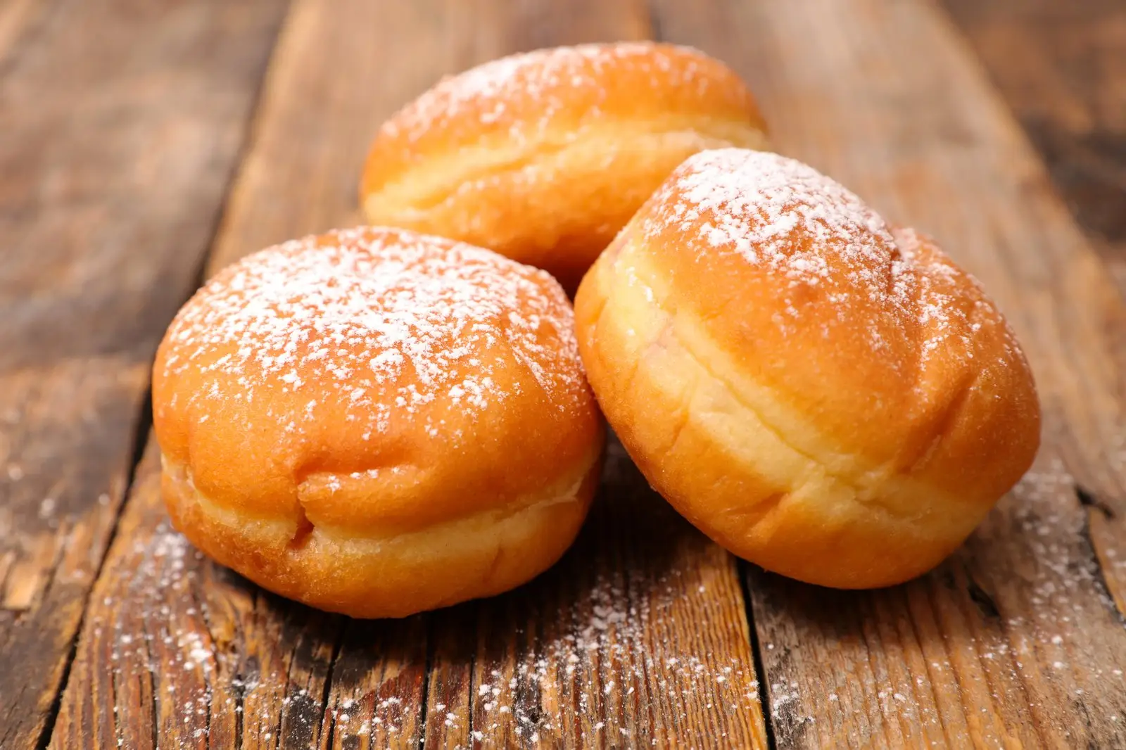 Drei Krapfen mit Puderzucker auf einem Holztisch