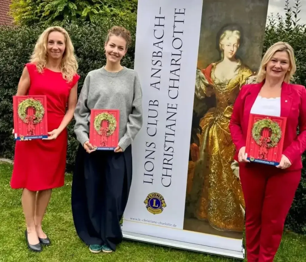 Drei Frauen mit dem roten Adventskalender 2025 vor dem Christiane-Charlotte-Banner