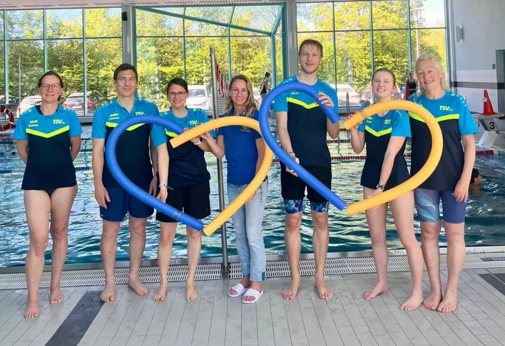 Schwimmtrainerinnen und Trainer formen mit Schwimmnudeln ein Herz
